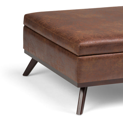 A close-up of the Owen Multifunctional Square Coffee Table Storage Ottoman features smooth brown leather upholstery, angled wooden legs, and a modern square design, shown on a white background.