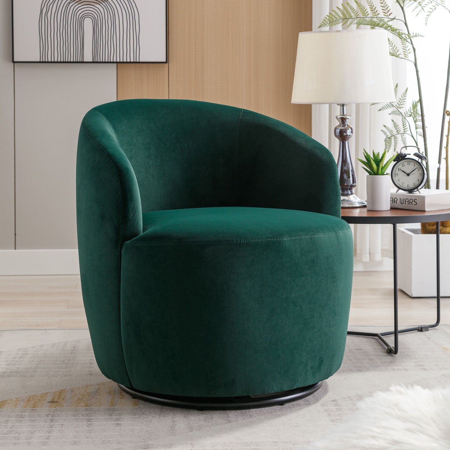 A Velvet Fabric Swivel Accent Armchair Barrel Chair with a powder-coated metal ring sits in a cozy living room by a side table, white lamp, clock, and plants. Abstract wall art decorates the space behind it.