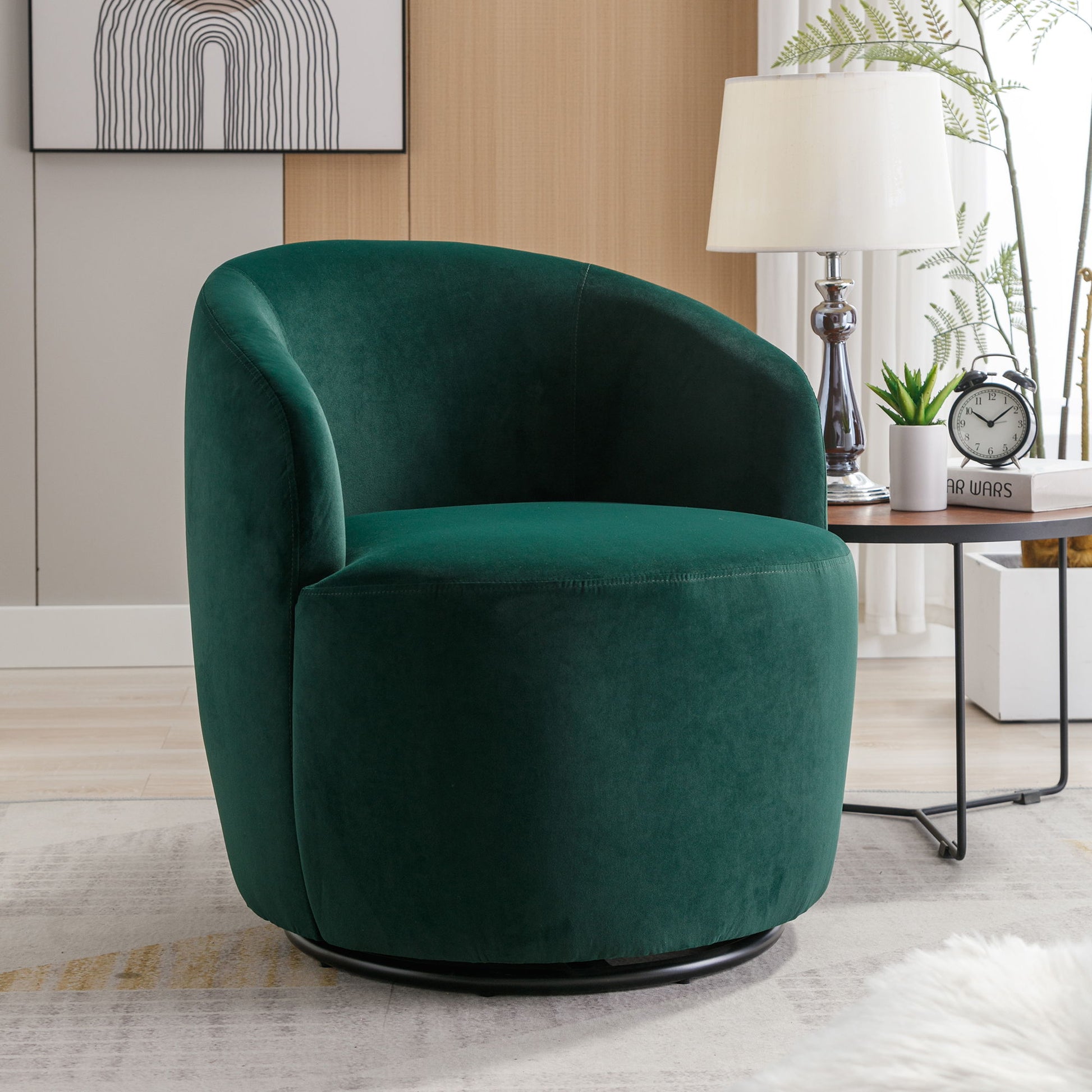 A Velvet Fabric Swivel Accent Armchair Barrel Chair with a powder-coated metal ring sits in a cozy living room by a side table, white lamp, clock, and plants. Abstract wall art decorates the space behind it.