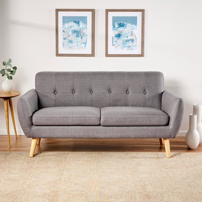 A Modern Loveseat Sofa With Button Tufted Backrest sits against a white wall, flanked by a round side table with a plant and white vases. Two abstract blue and white artworks hang above the sofa.