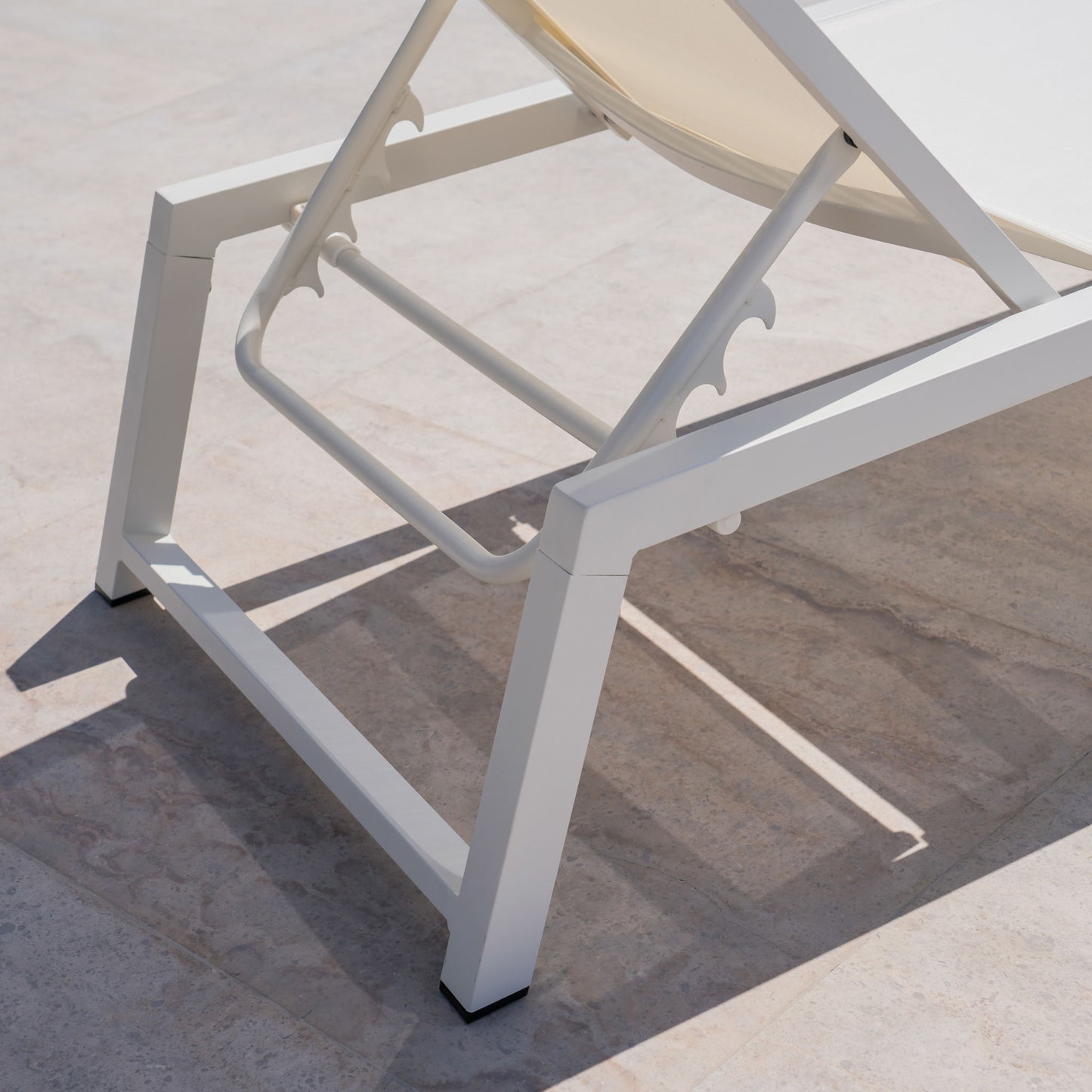 Close-up of the Myers - Modern Chaise Lounge Set with an adjustable mesh back, featuring a white metal frame and beige seat, casting a shadow on a light stone patio.