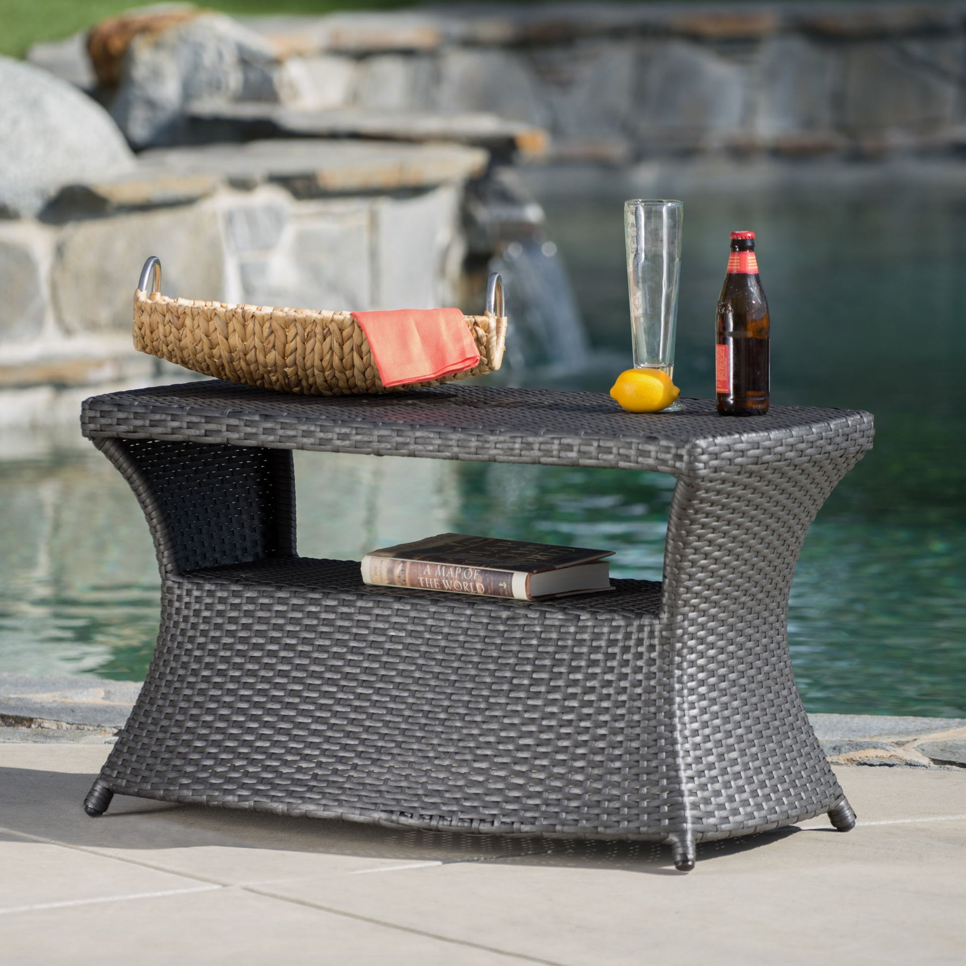 By the pool, the Berkeley - Chaise Lounge Side Table holds a tray with an orange napkin, empty glass, beer bottle, and lemon on top. A book is placed on its lower shelf.