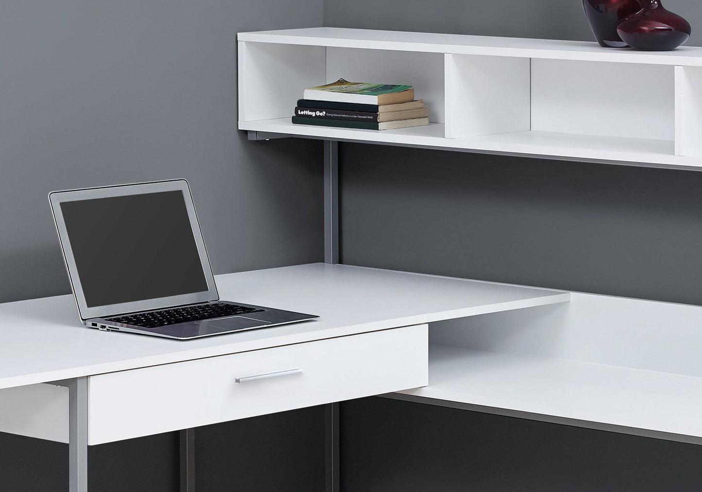 A contemporary L-shaped computer desk with storage drawers, perfect for a home office setup with a laptop, books, and decor items.