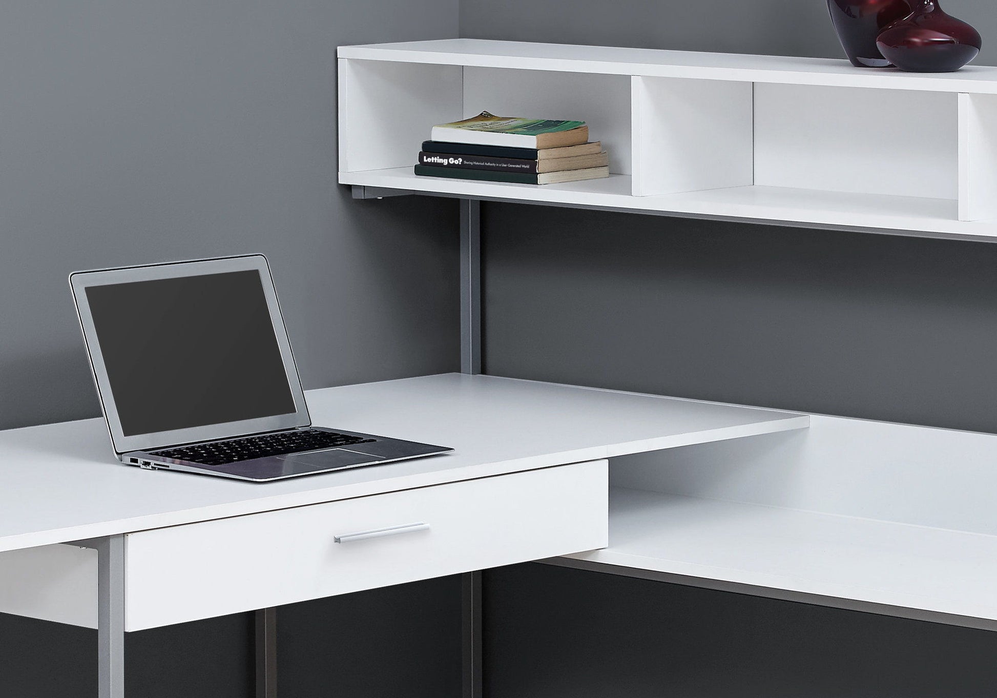 A contemporary L-shaped computer desk with storage drawers, perfect for a home office setup with a laptop, books, and decor items.