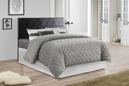 A modern bedroom with the Nova headboard in black, gray quilted bedding, striped pillows, light-colored walls, framed artwork, wooden floors, and a shaggy beige rug.