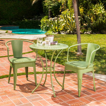The Ambrosia 3 Piece Bistro Set with leaf motif tops and seats features a green metal patio table and two matching chairs on a brick patio by the pool, topped with glasses of water and a potted plant amidst lush greenery.
