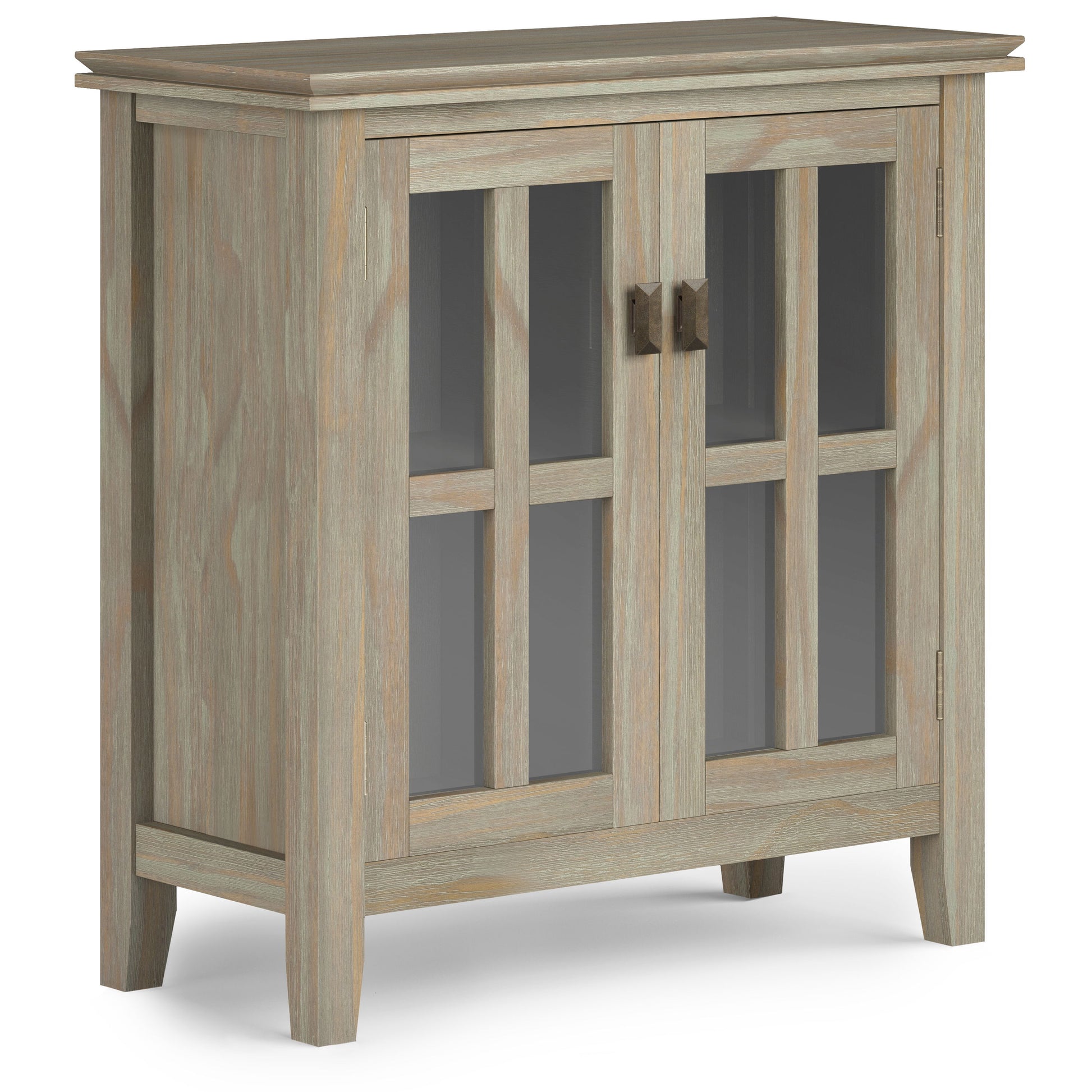 The Artisan - Handcrafted Low Storage Cabinet boasts a light, weathered wood finish, two glass-panel doors with metal handles, and stands on four short legs.