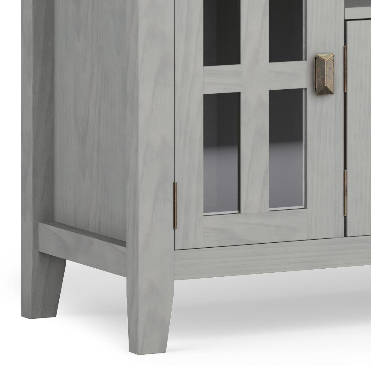 A close-up of the lower corner of the Artisan - TV Media Stand in light gray wood with glass-paneled doors, metallic handles, and four legs, set against a white background.