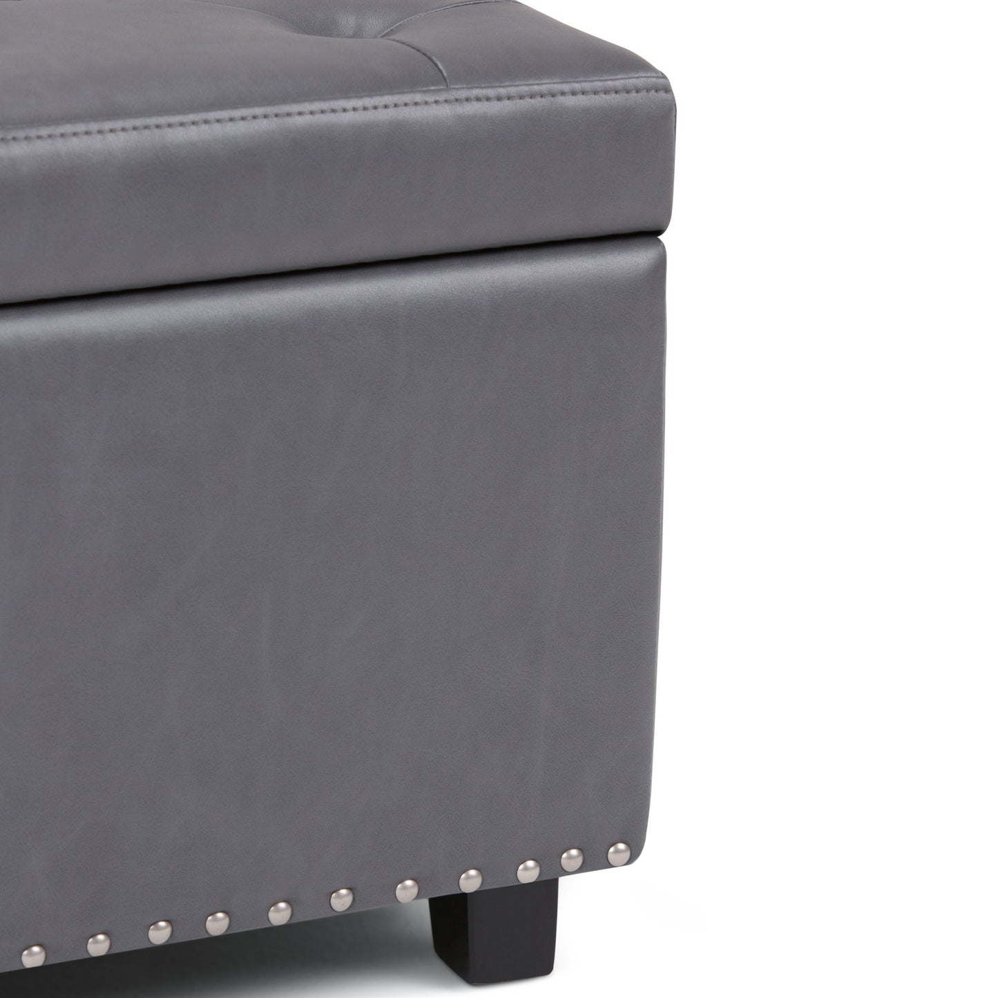 Close-up of the Hamilton Upholstered Storage Ottoman in gray, featuring silver nailhead trim, black wooden legs, and visible stitching on its tufted leather-like upholstery.