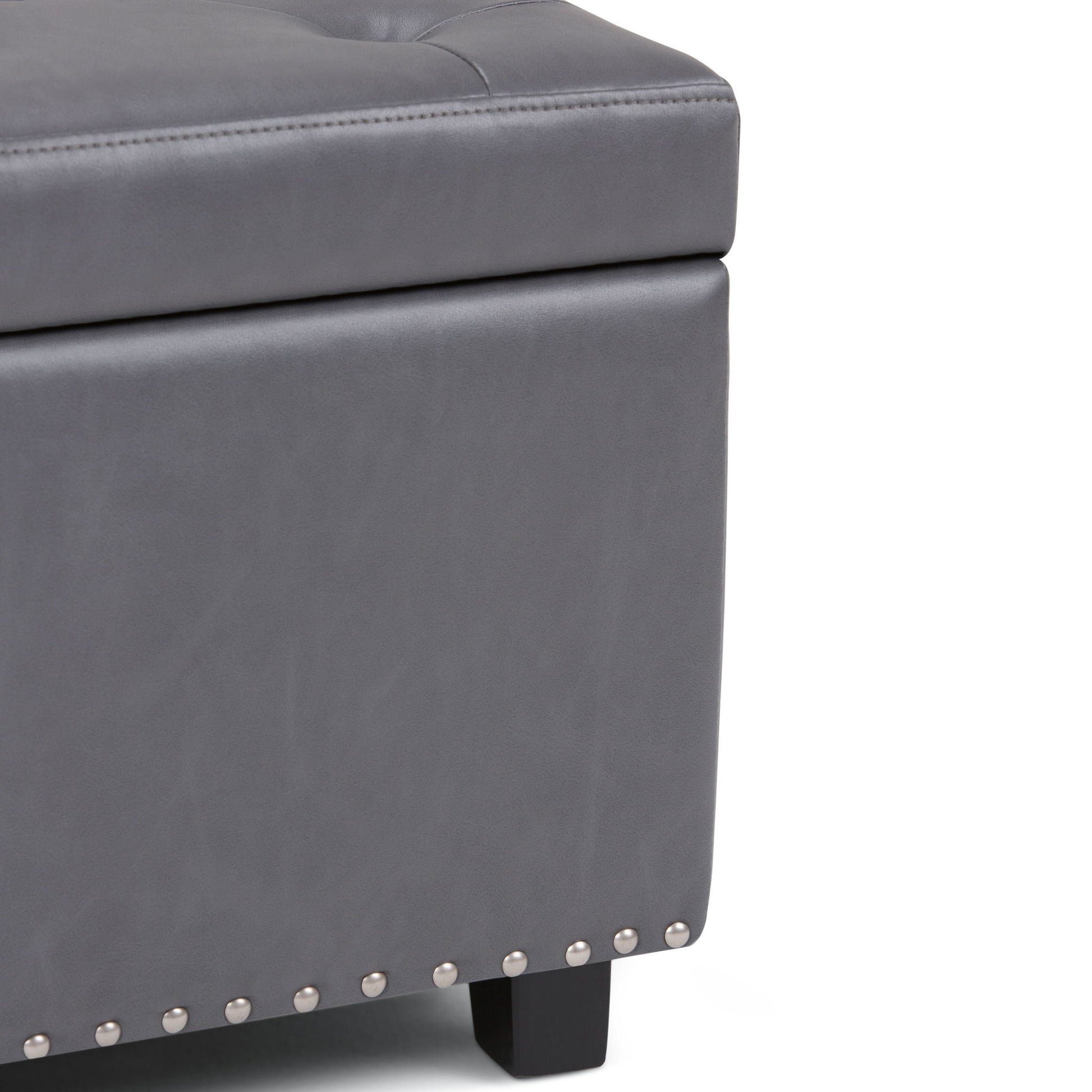 Close-up of the Hamilton Upholstered Storage Ottoman in gray, featuring silver nailhead trim, black wooden legs, and visible stitching on its tufted leather-like upholstery.