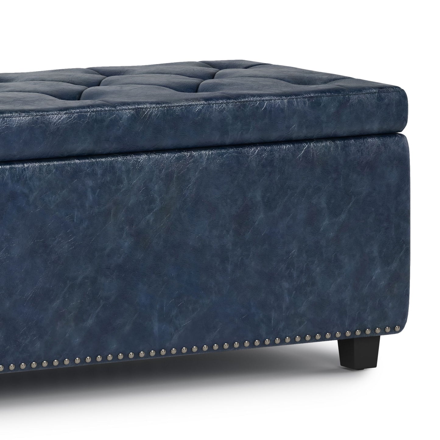 A close-up of the Hamilton Upholstered Storage Ottoman, featuring dark blue tufted leather, silver nailhead trim, and short black legs.