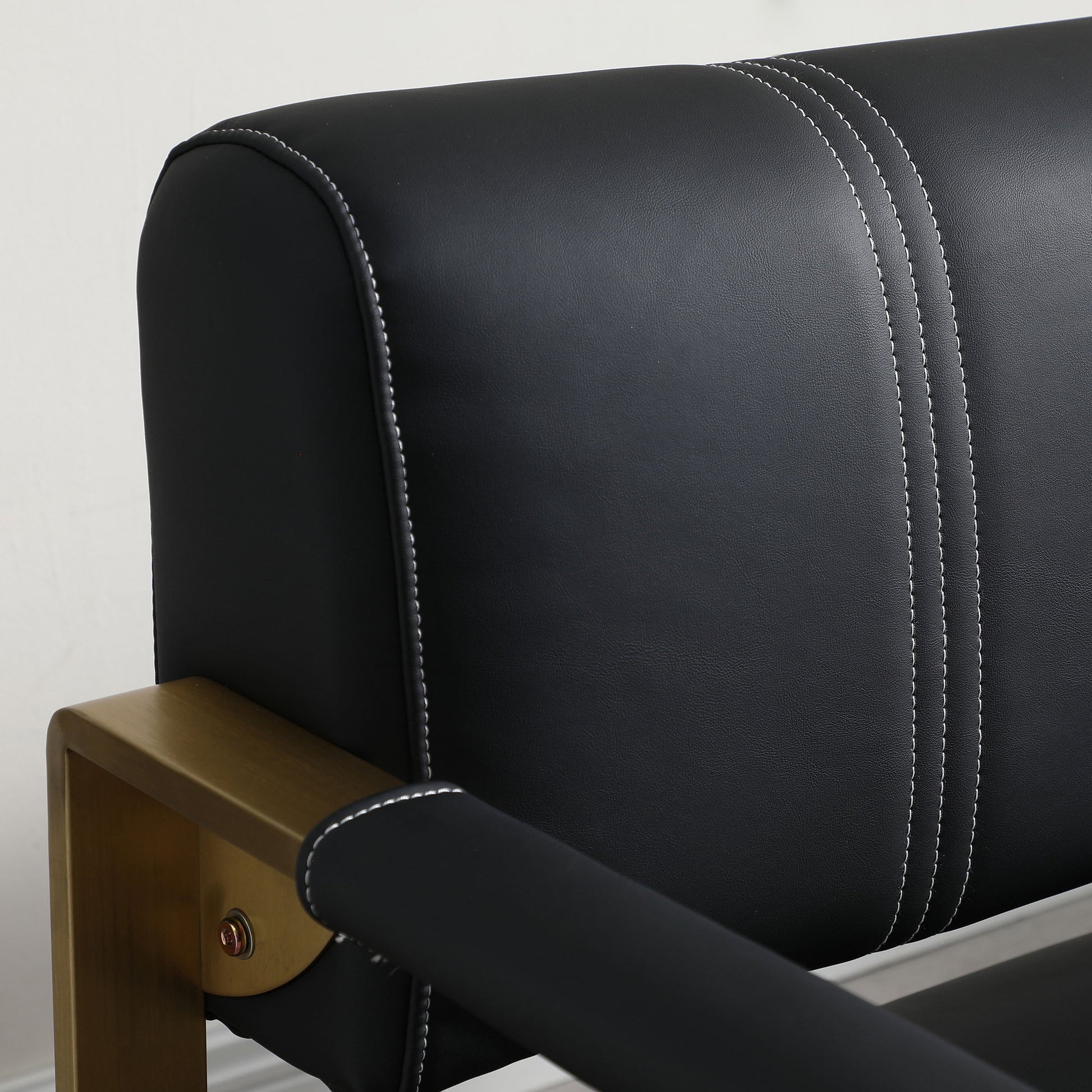 Close-up of the Modern Upholstery Accent Loveseat Sofa—a 2-seater with a black leather backrest featuring white stitching and sleek golden metal arms, set against a plain white wall.