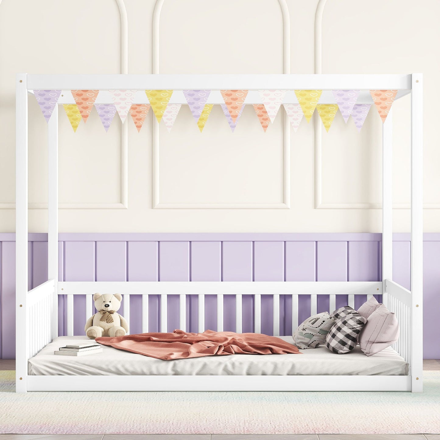 A Canopy Frame Floor Bed With Fence, Guardrails, in white, is adorned with pastel bunting. It features a pink blanket, two plaid pillows, and a teddy bear, set against pastel purple and cream walls.