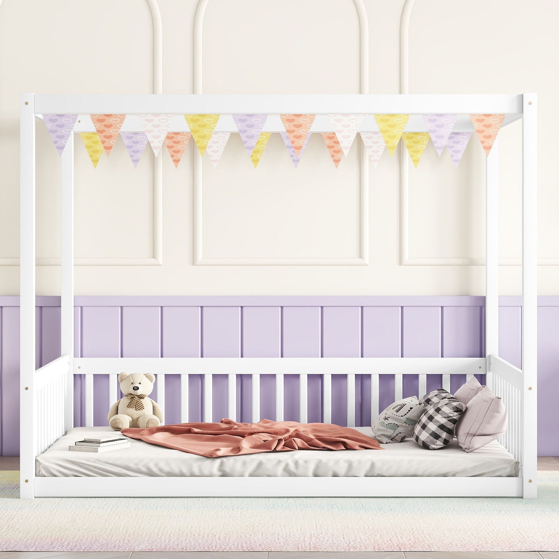 A Canopy Frame Floor Bed With Fence, Guardrails, in white, is adorned with pastel bunting. It features a pink blanket, two plaid pillows, and a teddy bear, set against pastel purple and cream walls.