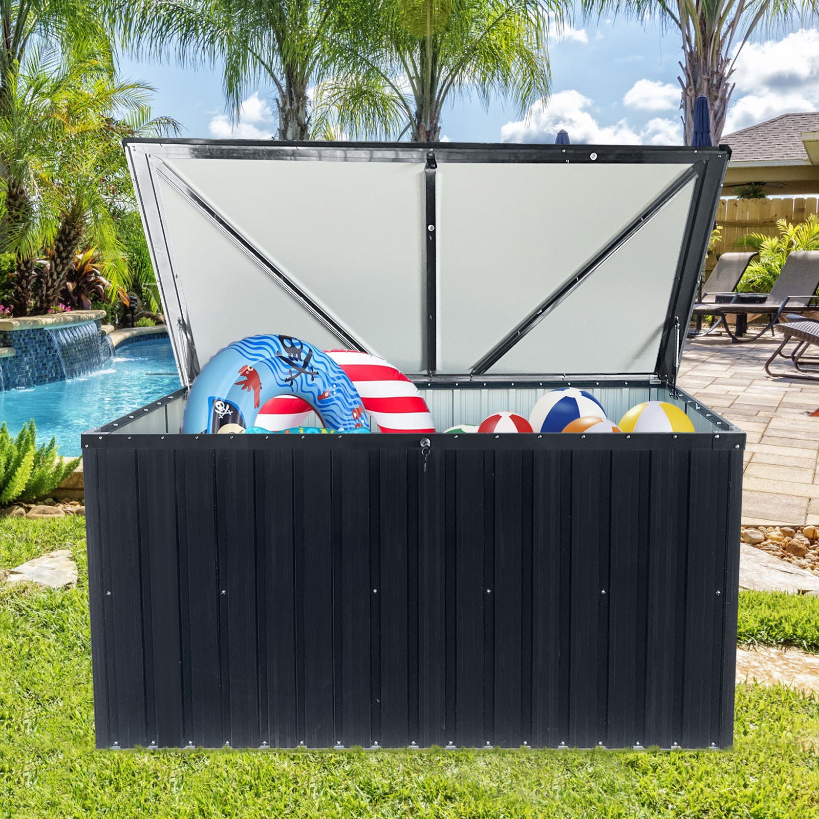 The Metal Storage Box Store Large Out Door Use - Black sits open in a backyard by the pool, surrounded by palm trees and patio furniture, with pool toys like inflatable rings and beach balls visible inside.