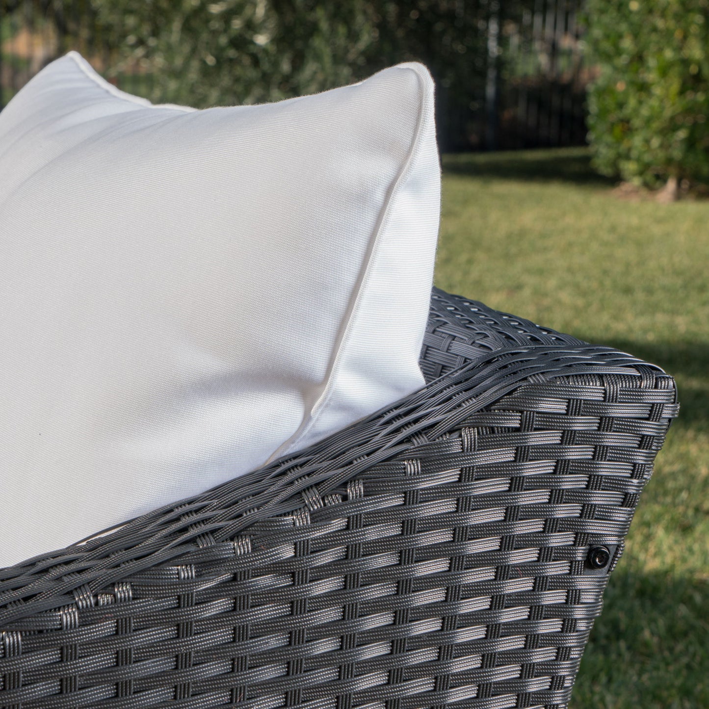 A close-up of the Antibes Armchair with water resistant cushions, featuring a gray wicker design and a large white cushion, set on a grassy lawn with lush green foliage in the background.