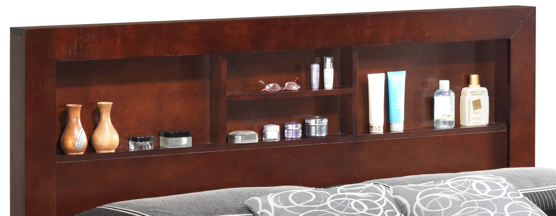 The Bed With Transitional Design Stylish features a wooden headboard with built-in shelves displaying vases, jars, lotion bottles, skincare products, glasses, and other small items above a bed with gray and white patterned pillows.
