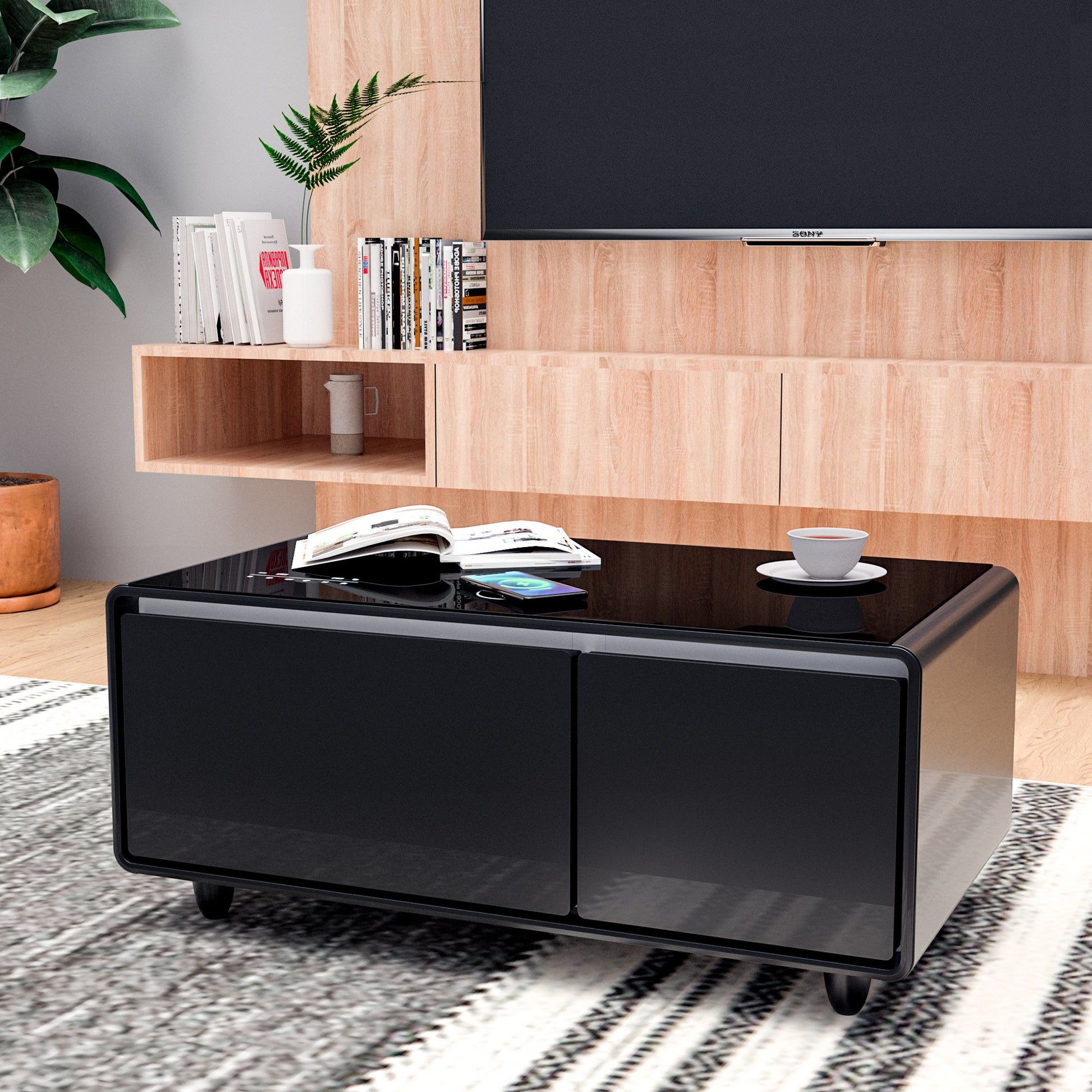 A modern living room features the Modern Smart Coffee Table With Built-In Fridge, Bluetooth Speaker, wireless charging, touch control panel, USB interface, outlet protection, and atmosphere light, with bookshelves and a large flat-screen TV in the background.
