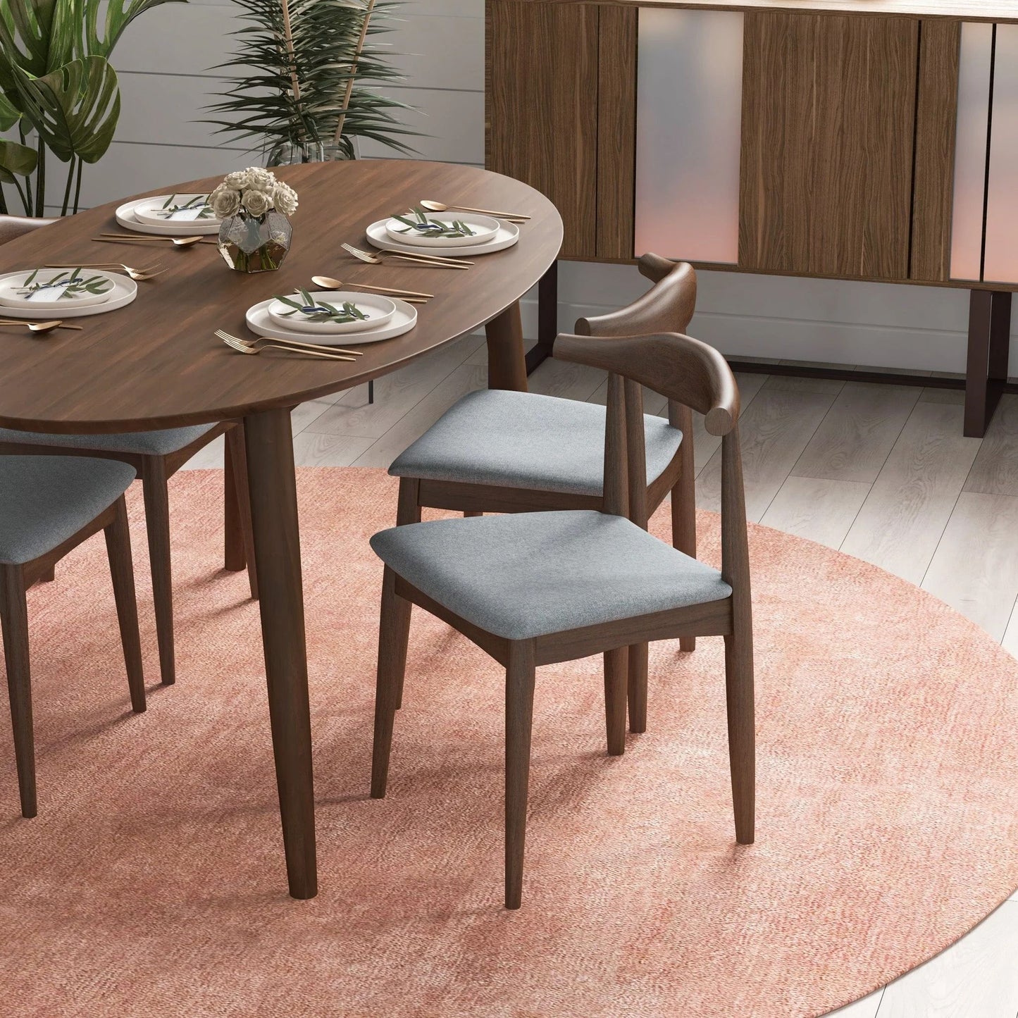 A modern dining area with a wooden table for four, Destiny - Modern Dining Chairs (Set of 2) in gray, a small flower centerpiece, and a sideboard on a light pink circular rug over light wood flooring.