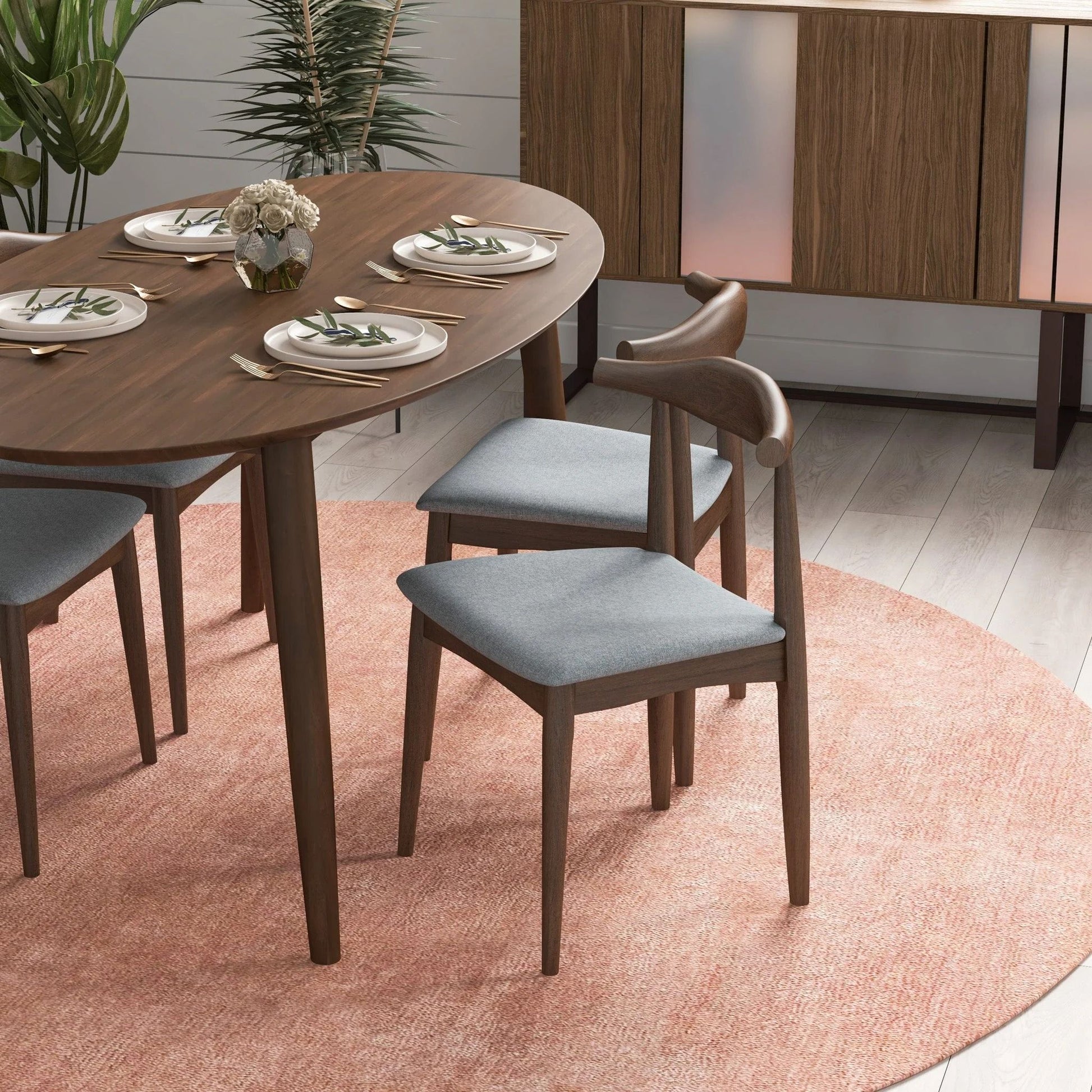 A modern dining area with a wooden table for four, Destiny - Modern Dining Chairs (Set of 2) in gray, a small flower centerpiece, and a sideboard on a light pink circular rug over light wood flooring.