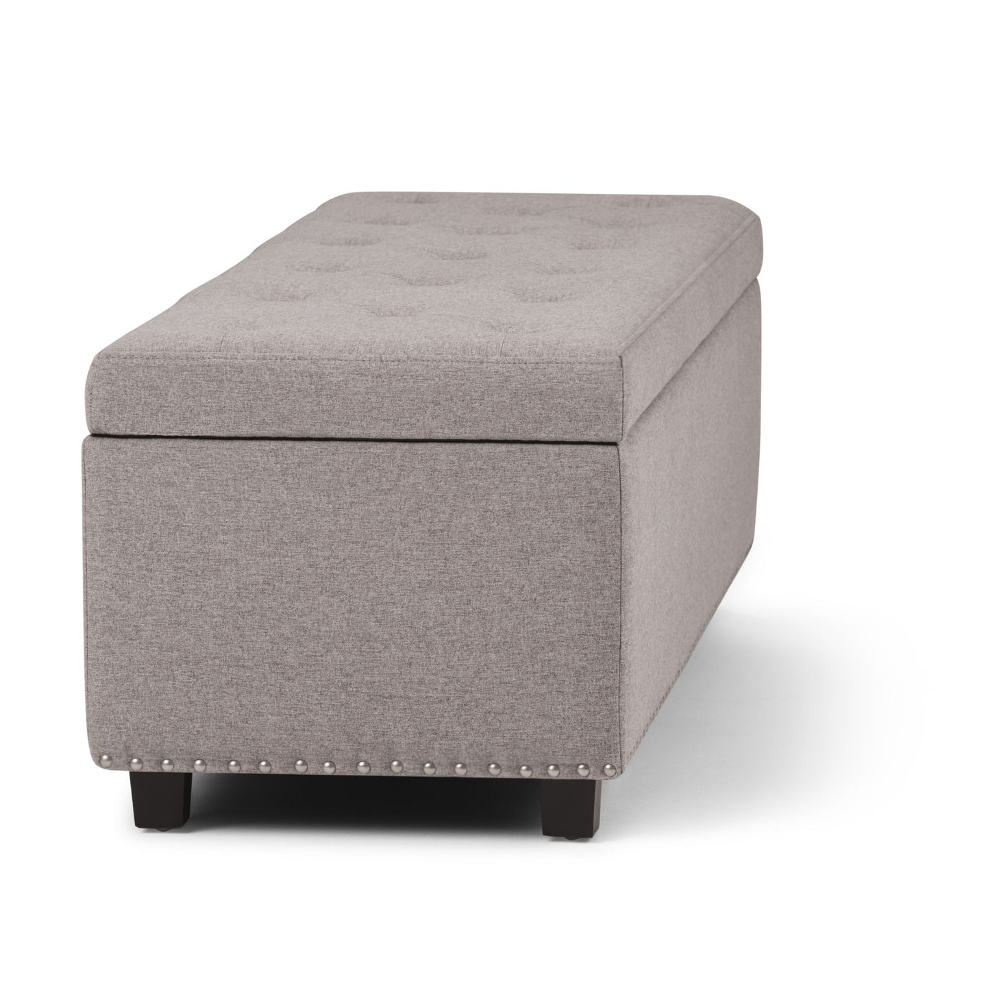 The Hamilton Upholstered Storage Ottoman features a rectangular, light gray tufted top, dark wooden legs, and silver nailhead trim along the bottom edge, displayed against a white background.