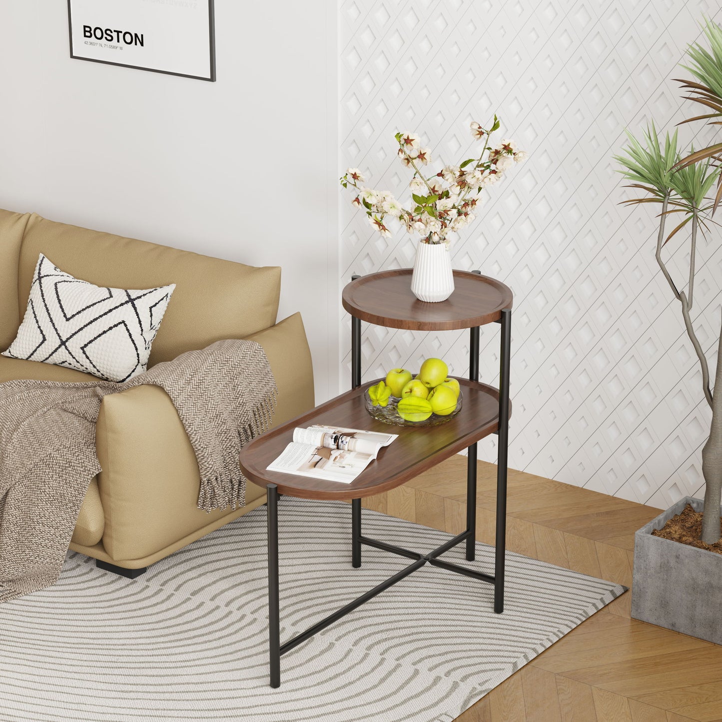 A modern living room features a beige sofa, patterned pillow, and blanket. In front stands a Round Coffee Table With Storage Tray 2 Tier Oval End Tables Wooden Small Side Table holding magazines, green apples, and a white vase with flowers.