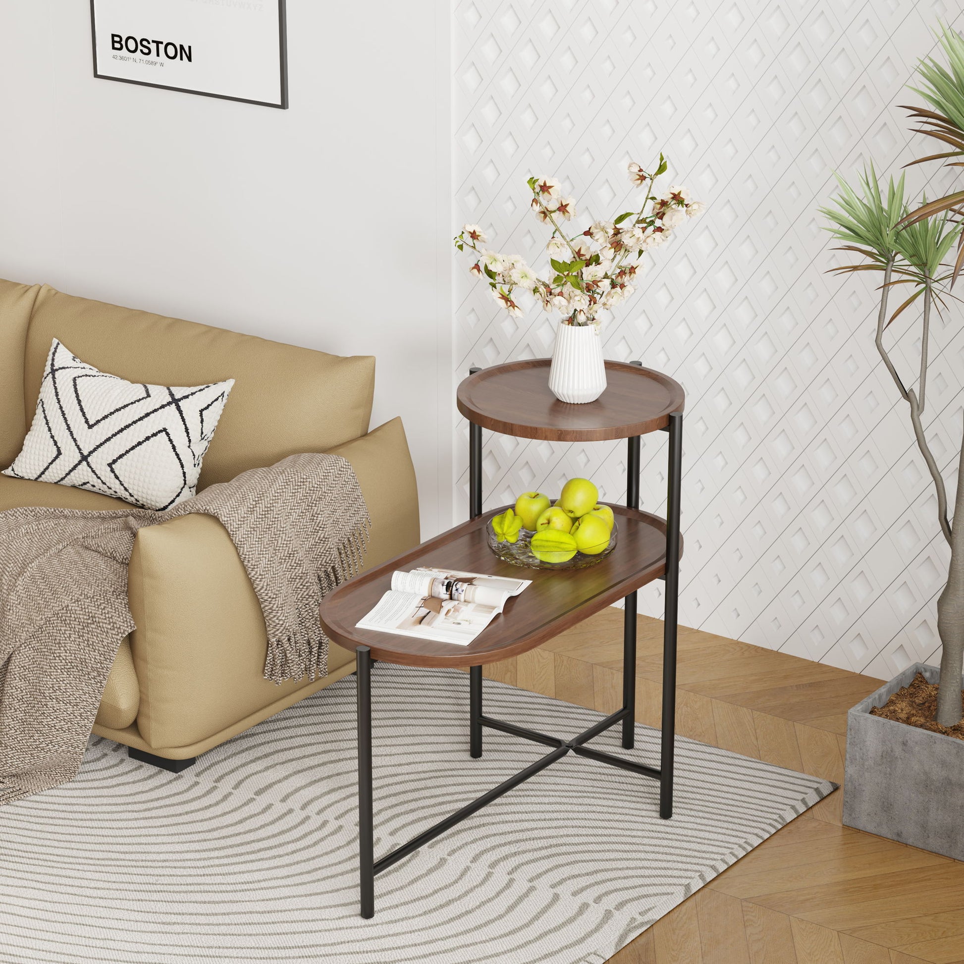 A modern living room features a beige sofa, patterned pillow, and blanket. In front stands a Round Coffee Table With Storage Tray 2 Tier Oval End Tables Wooden Small Side Table holding magazines, green apples, and a white vase with flowers.
