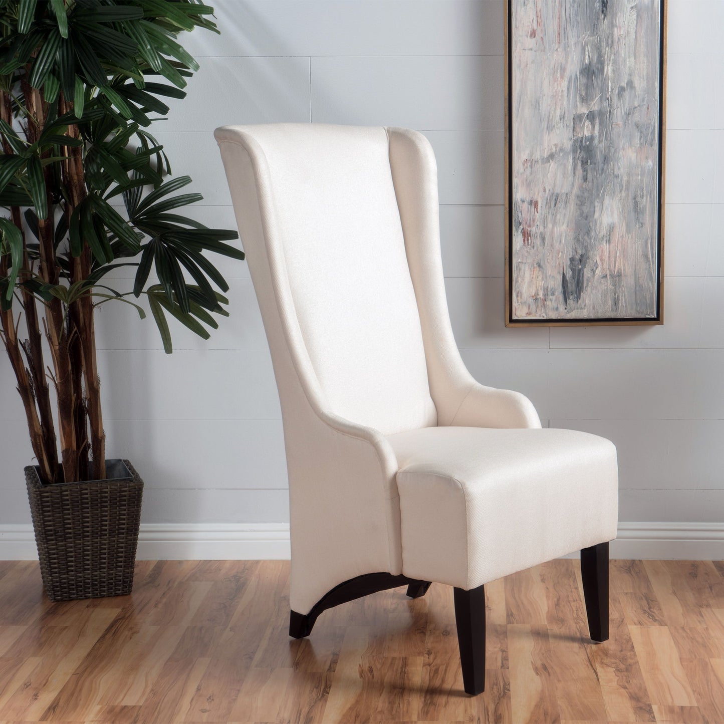 A set of 2 Alight Upholstered Dining Chairs with high backs and birch wood legs stands on a wooden floor by a potted plant and an abstract painting against a light gray wall.