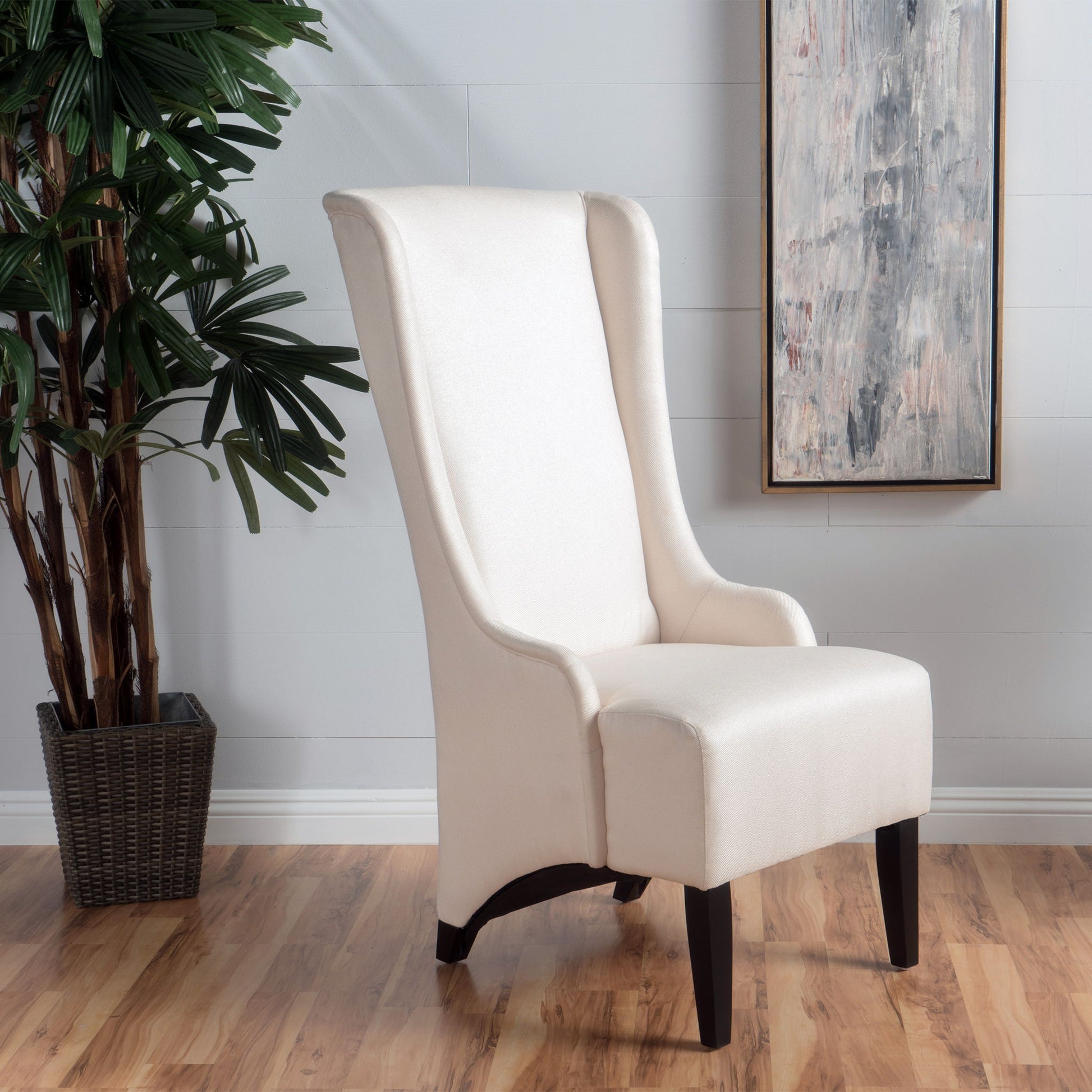 A set of 2 Alight Upholstered Dining Chairs with high backs and birch wood legs stands on a wooden floor by a potted plant and an abstract painting against a light gray wall.