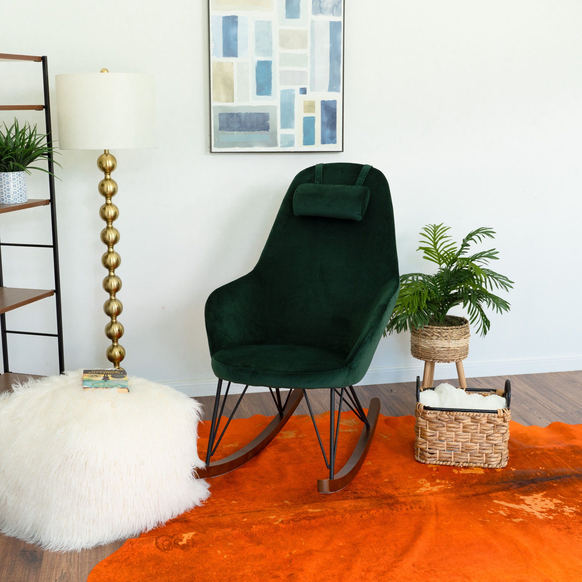 A modern living space with the Chloe Mid Century Modern Rocker chair in dark green, a fluffy white ottoman, gold floor lamp, potted plant, woven basket, and abstract wall art atop an orange rug on wood flooring.