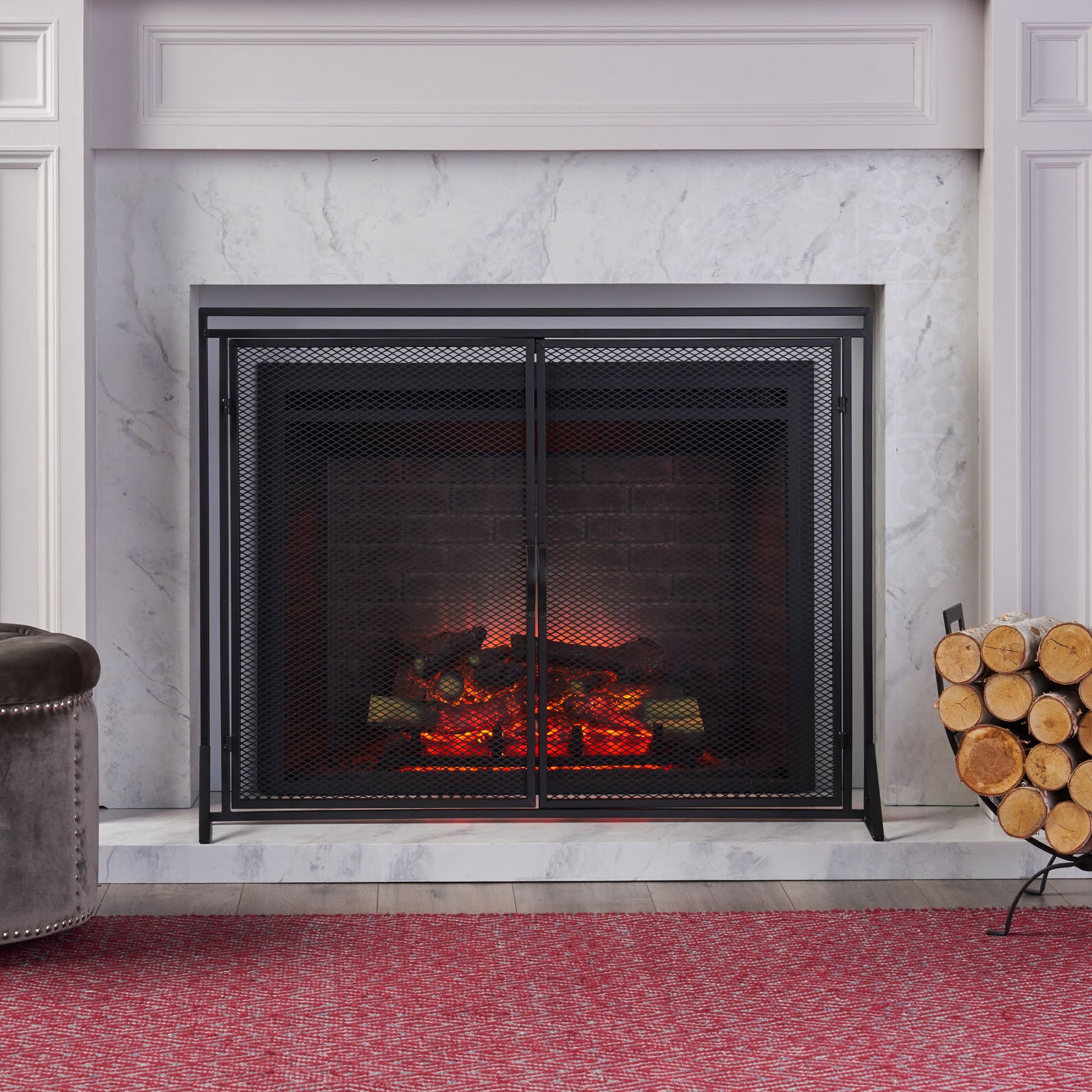 The Samantha - Iron Fireplace Screen 2 Door Design stands in front of a modern fireplace with glowing logs, marble surround, firewood stacked on the right, and a red textured rug covering the floor in front.