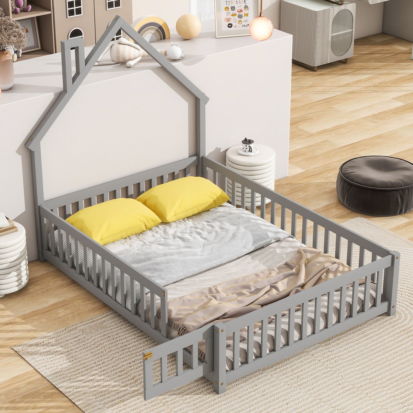 The House-Shaped Headboard Floor Bed With Fence in gray features a low gate, two yellow pillows, gray blanket, and beige throw, set on a light rug in a bright modern children’s room with wooden floors.