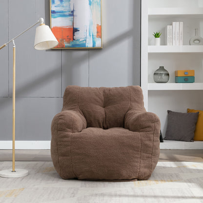 A Soft Teddy Fabric Tufted Foam Bean Bag Chair with teddy fabric rests on a light rug beside a modern floor lamp, with a white shelving unit and abstract artwork in the background.