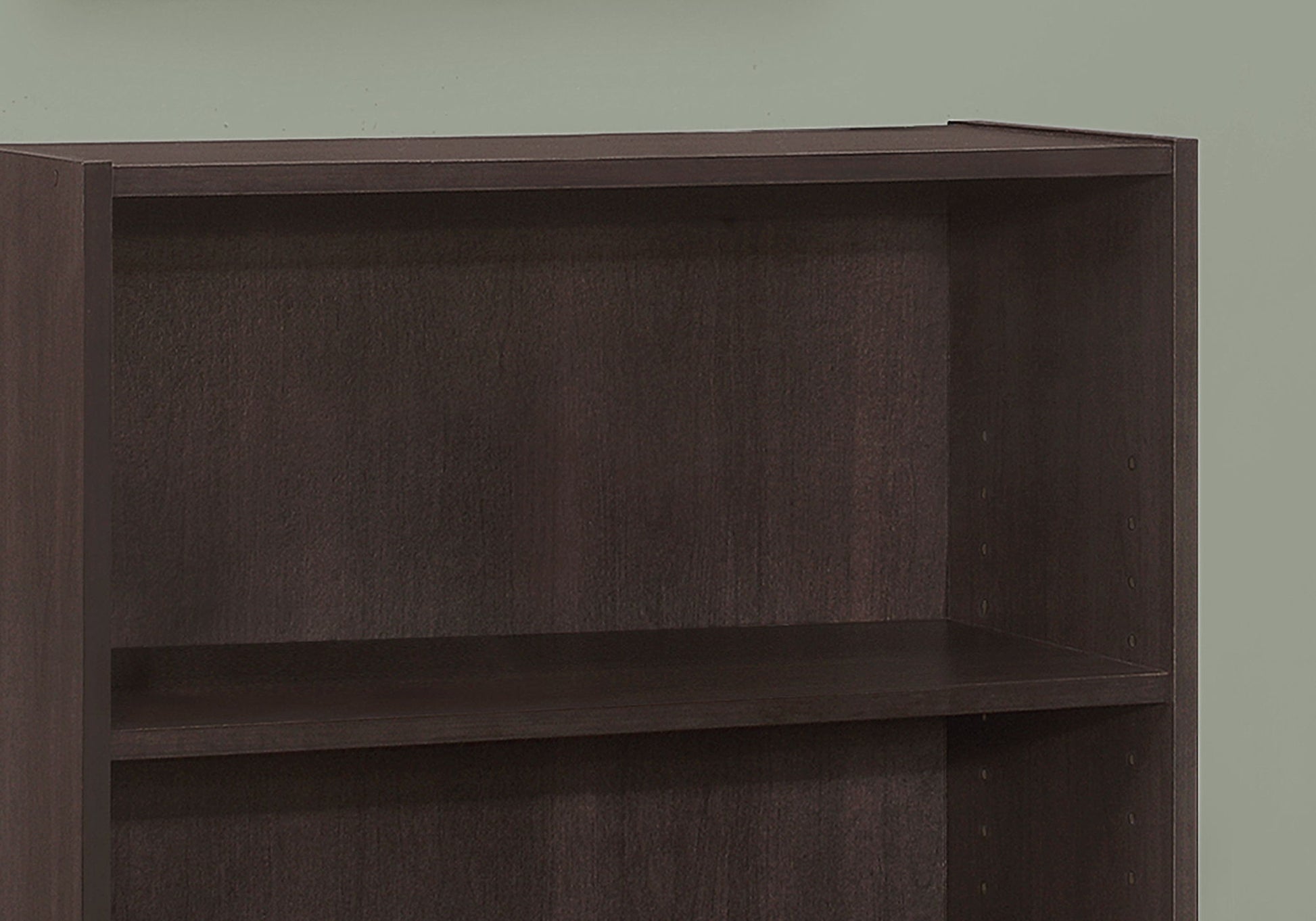 A close-up of an empty dark brown 4-tier transitional bookshelf, ideal for office use, placed against a plain light green wall.