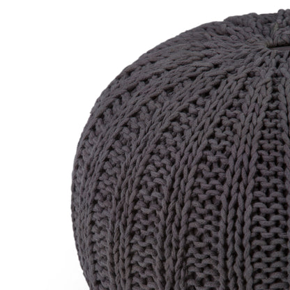 Close-up of the Shelby - Handcrafted Hand Knit Round Pouf in dark gray, featuring thick yarn and a textured ribbed pattern, partially visible against a white background.