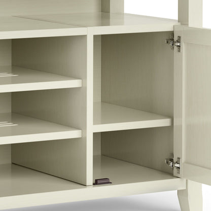 The Amherst - TV Media Stand, Handcrafted, features a cream-colored wood-finish cabinet with metal door hinges on the right, revealing two shelves inside—one placed lower—and a small black item in the bottom right corner.