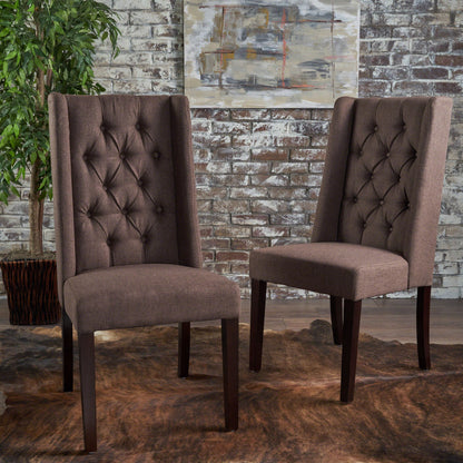 Two Sophisticated Tufted Dining Chairs with high back designs and dark wooden legs sit on a brown rug before a whitewashed brick wall, complemented by a potted plant and abstract art in the background.