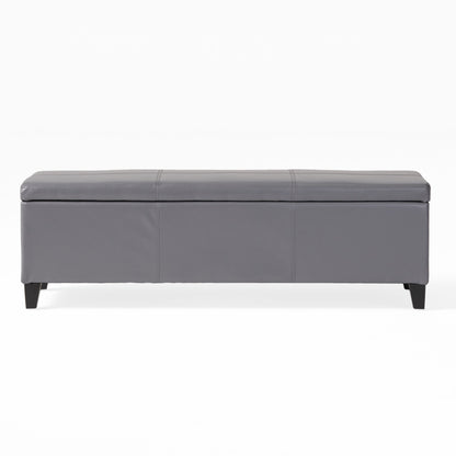 The Glouster - Contemporary Storage Ottoman features a rectangular gray design with a padded top, stitched details, and short black legs, shown against a plain white background.