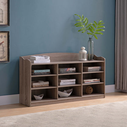 An Entryway Shoe Storage Bench with nine storage shelves stands by a blue wall, holding shoes, baskets, and decor. On top are stacked books, a glass vase with green leaves, and a white lantern.