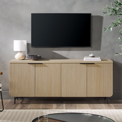 A flat-screen TV is mounted on a gray wall above the Modern Fluted Door Minimalist Storage Sideboard, which displays a white lamp, a round dark tray, and stacked books. A nearby plant and table are also visible.