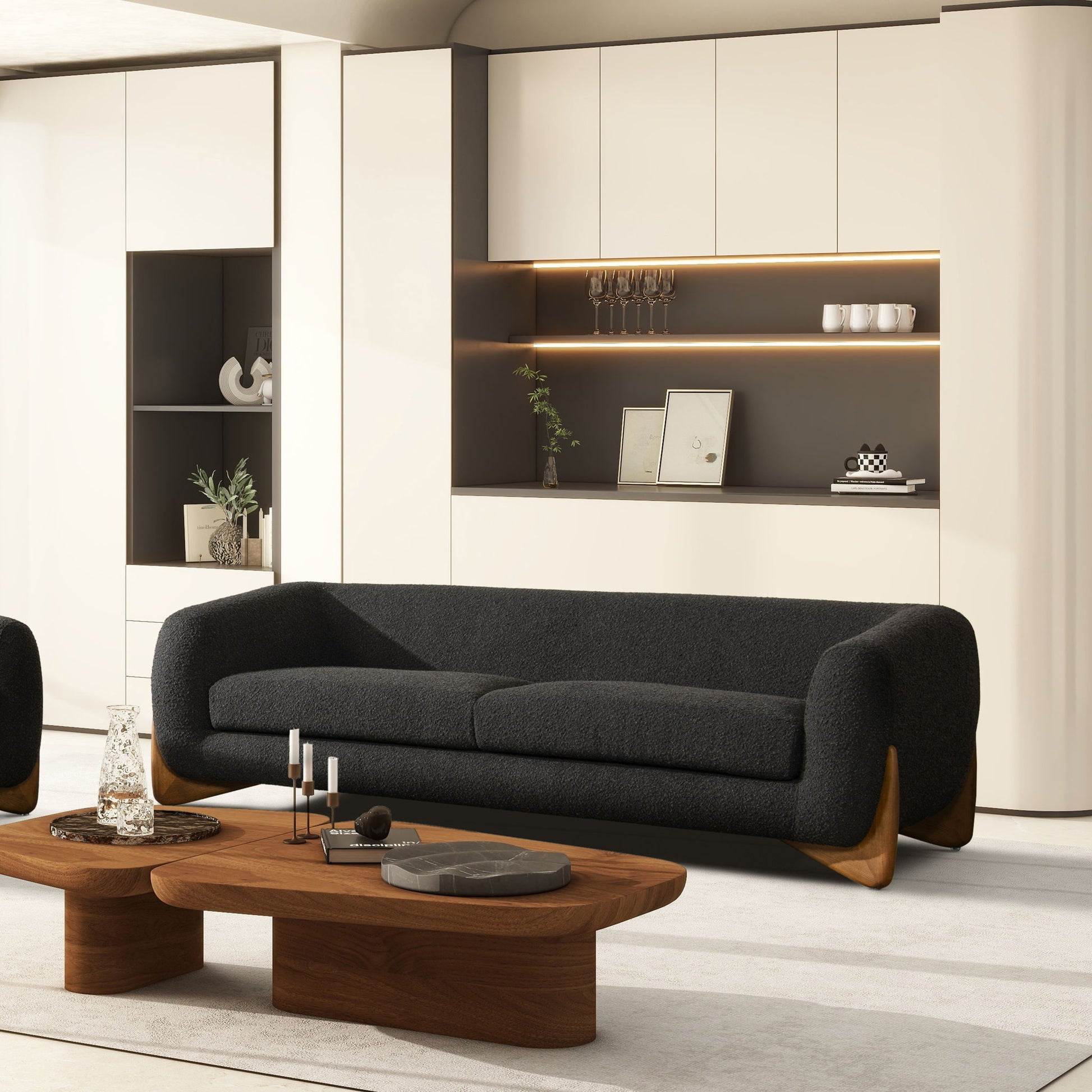 A modern living room featuring the Alpine Luxurious Upholstery Sherpa Sofa in black, two wooden coffee tables, built-in beige cabinets, open shelves with decor, and warm accent lighting for a minimalist and stylish look.