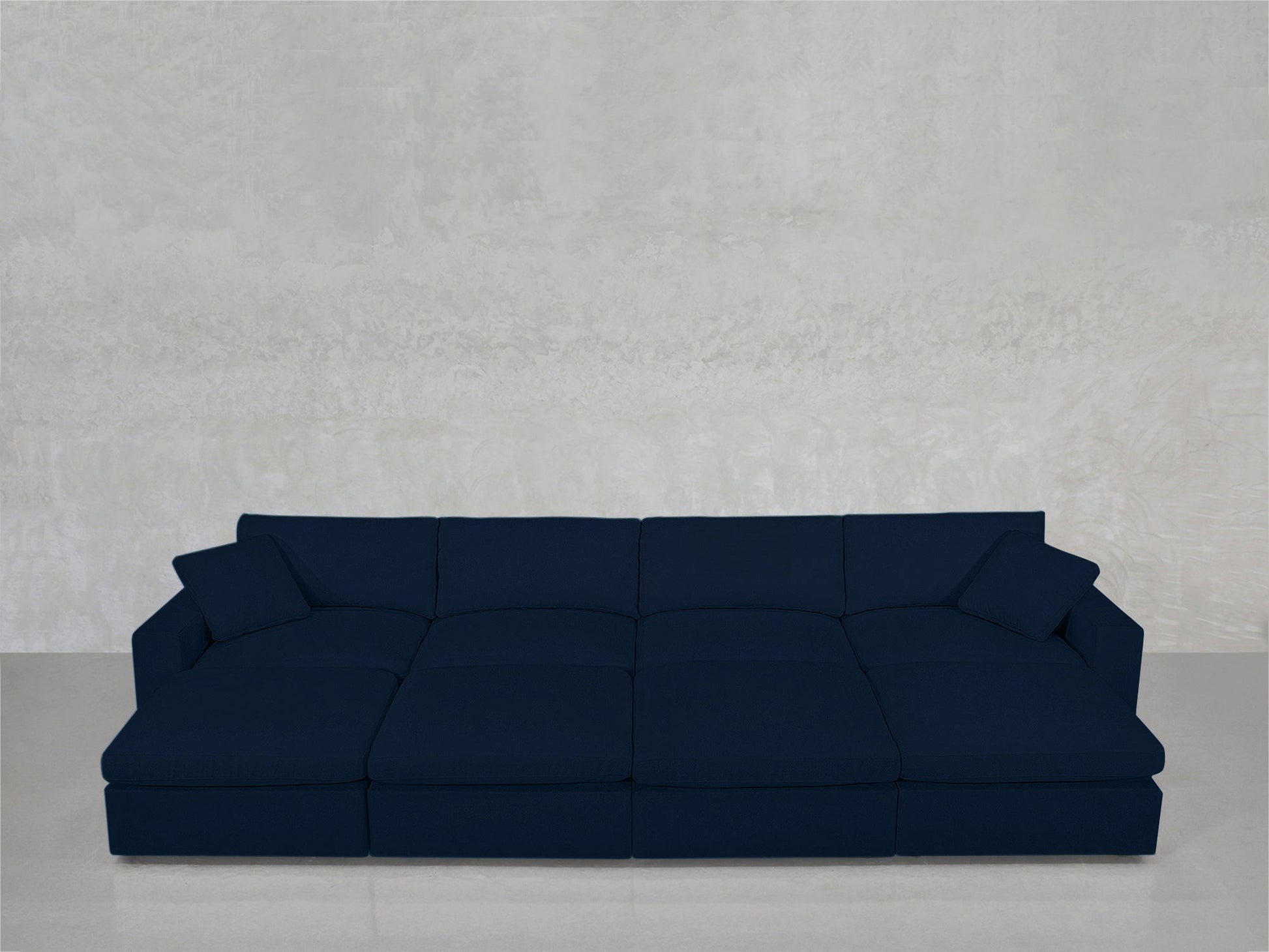 An 8-Seat Modular Daybed in dark blue, with two matching cushions, sits against a light gray textured wall on a glossy floor.
