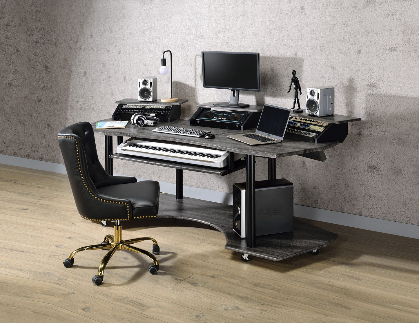 A modern home studio setup features the Eleazar Music Recording Studio Desk in wood, paired with a black and gold office chair, holding a computer monitor, speakers, audio equipment, keyboard piano, headphones, and a laptop on a light wood floor.