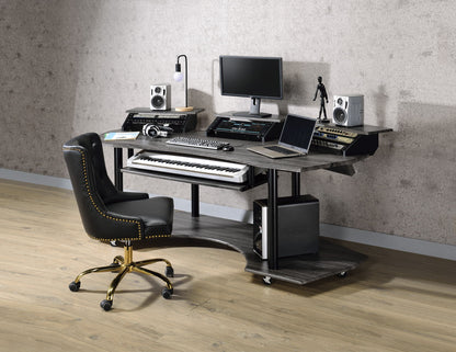 A modern home studio setup features the Eleazar Music Recording Studio Desk in wood, paired with a black and gold office chair, holding a computer monitor, speakers, audio equipment, keyboard piano, headphones, and a laptop on a light wood floor.