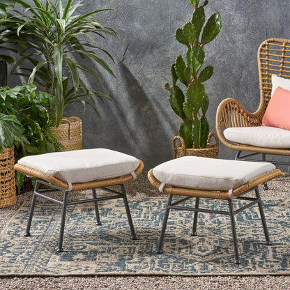 Two Outdoor Modern Boho Wicker Ottomans With Cushions (Set of 2) rest on a patterned rug next to a wicker chair with a coral pillow, surrounded by green potted plants and set against a textured gray wall.