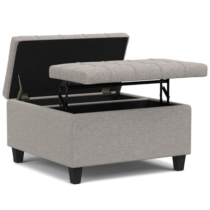 The Harrison Upholstered Coffee Table Storage Ottoman features a light gray tufted top that opens on metal hinges to reveal spacious storage inside, and stands on four short black legs.
