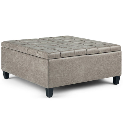 The Harrison Upholstered Coffee Table Storage Ottoman features a square, tufted design in light gray with dark wooden legs and a cushioned top, shown against a white background.