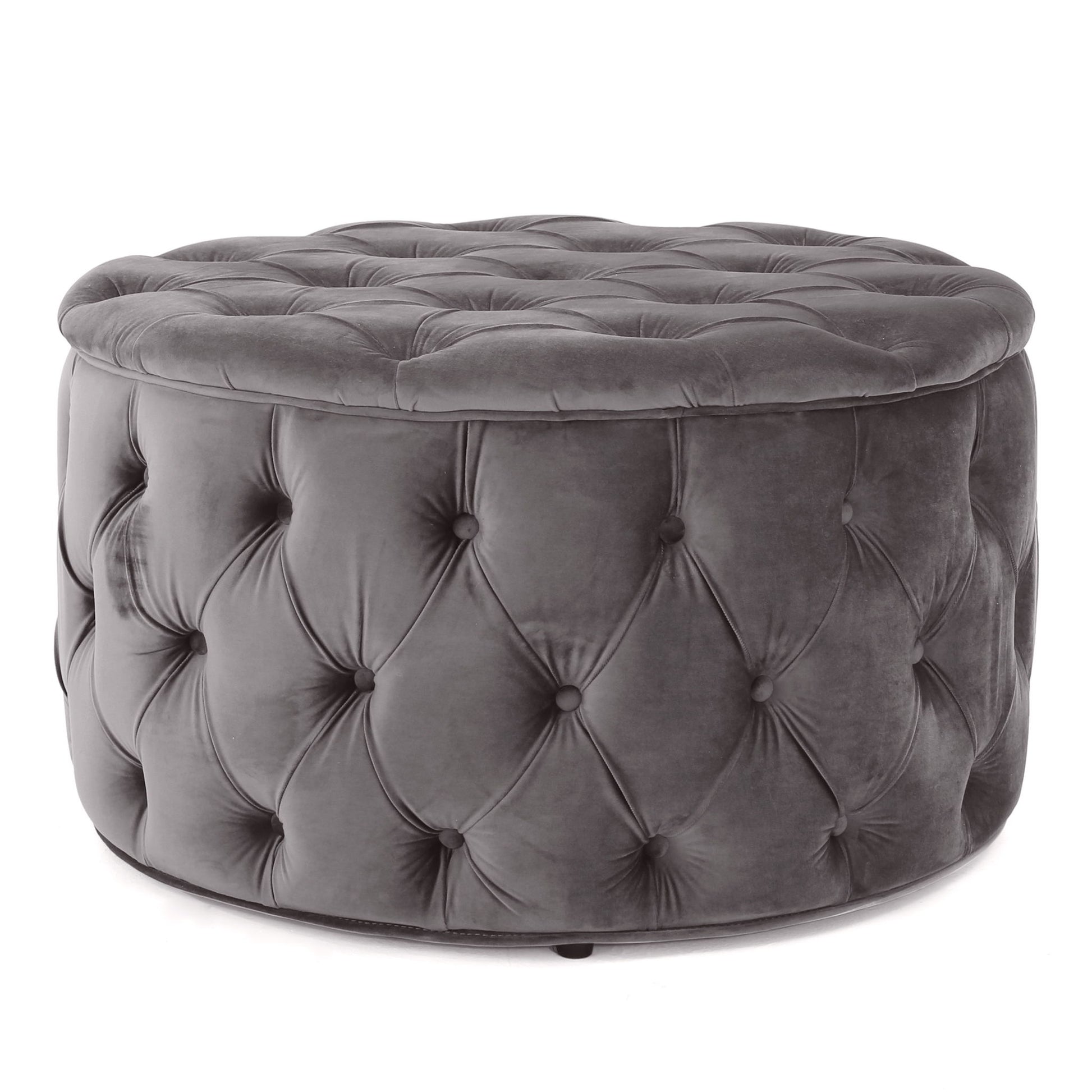 The Modern Glam Ottoman Velvet is a round ottoman, upholstered in dark gray velvet with a plush cushioned top and button-tufted sides.