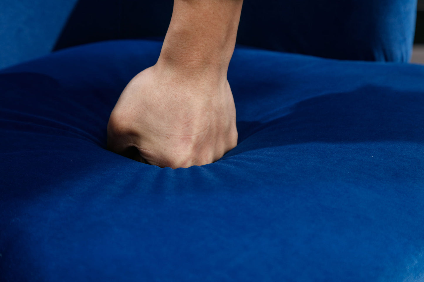 A hand presses down firmly on the plush Velvet Fabric Swivel Accent Armchair Barrel Chair With Powder Coating Metal Ring, making the deep blue fabric visibly indent under pressure.