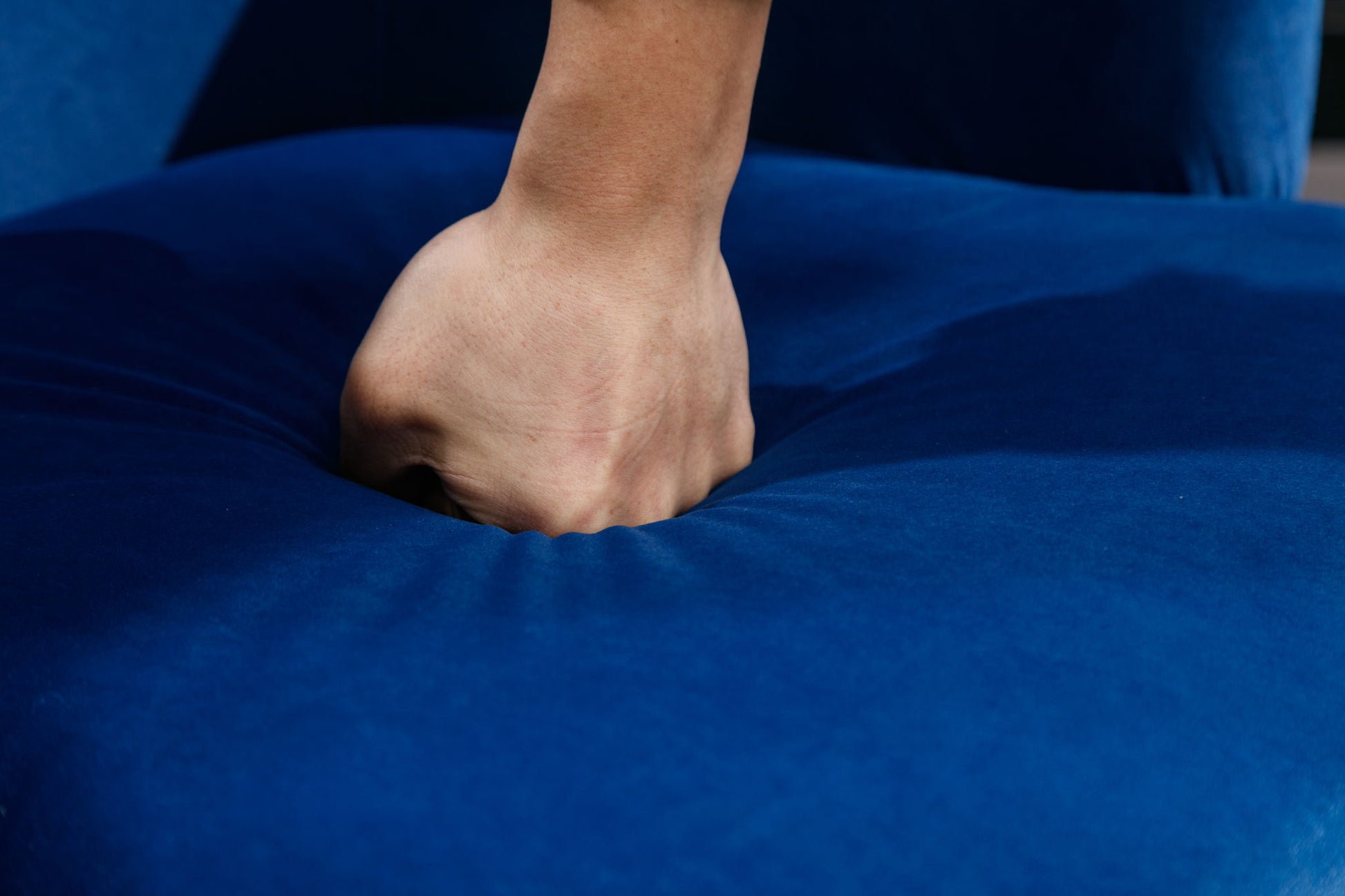 A hand presses down firmly on the plush Velvet Fabric Swivel Accent Armchair Barrel Chair With Powder Coating Metal Ring, making the deep blue fabric visibly indent under pressure.